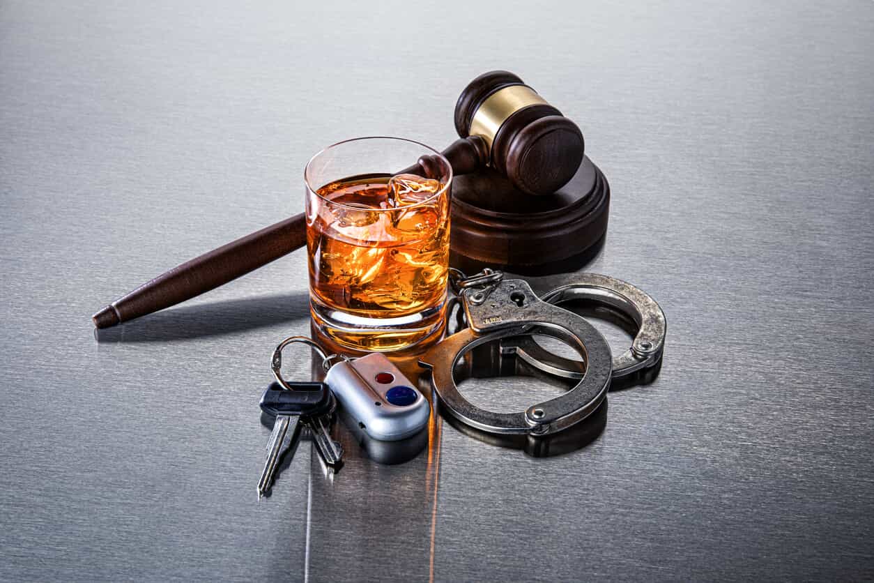 Gavel next to alcohol next to handcuffs next to car keys